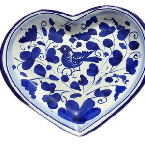 May include: A heart-shaped ceramic dish with a blue and white floral design. A blue bird is perched on a branch in the centre of the dish.