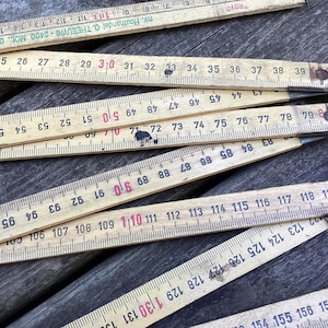 May include: A collection of old wooden folding rulers, showing signs of wear. The rulers are light yellow with black and red markings, including numbers and measurement increments in centimetres. The rulers are angled.