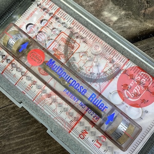 May include: A clear plastic ruler with a metal measuring tool inside. The ruler has a blue inscription that reads "Multipurpose Ruler" and "Patent No. 20222". The ruler also has a protractor and a compass.