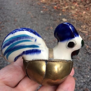 May include: A ceramic rooster figurine with blue and white painted details. The rooster is sitting on a gold metal base.