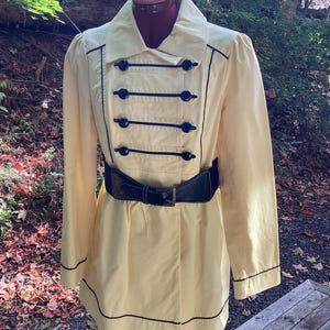 May include: A yellow jacket with black trim and buttons. The jacket has a black belt with a silver buckle.