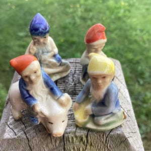 May include: Four ceramic figurines of gnomes, each with a different hat colour: blue, red, yellow, and orange. One gnome is riding a pig.