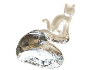 May include: A clear glass figurine of a cat sitting on a clear glass base. The cat is sitting upright with its tail curled around its body.