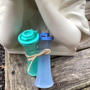 May include: Two plastic salt and pepper shakers, one teal and one light blue, tied together with twine. The shakers are on a wooden surface.