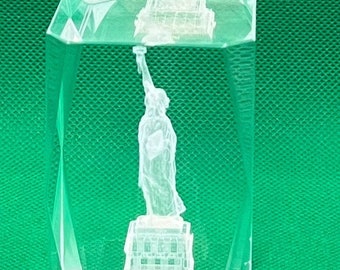 May include: A clear glass cube with a 3D etched image of the Statue of Liberty. The statue is white and the base is detailed with the base of the statue.