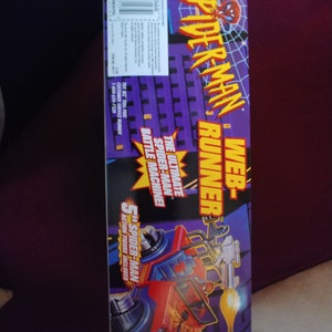 May include: A red and blue toy vehicle with a Spider-Man figure on the side. The vehicle has a web shooter and a battle machine. The box says "Web-Spider-Man Runner" and "The Ultimate Spider-Man Battle Machine!"