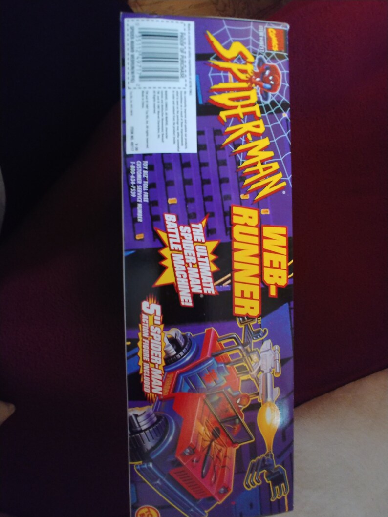 May include: A red and blue toy vehicle with a Spider-Man figure on the side. The vehicle has a web shooter and a battle machine. The box says "Web-Spider-Man Runner" and "The Ultimate Spider-Man Battle Machine!"