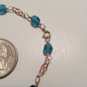 May include: A gold chain bracelet with blue gemstone beads. The chain features a delicate, intricate design.