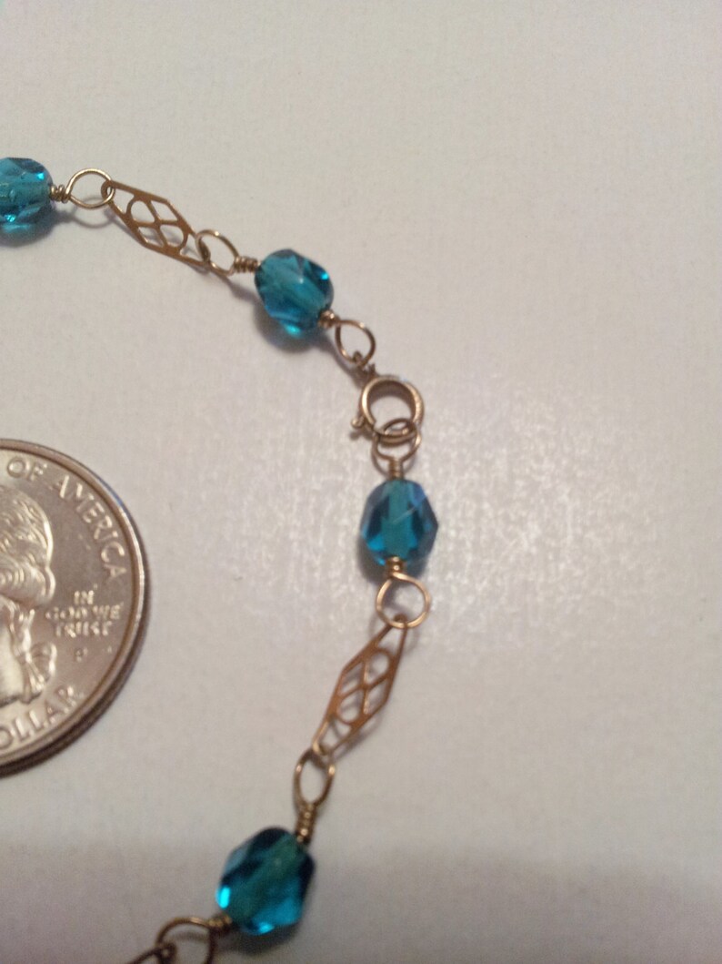 May include: A gold chain bracelet with blue gemstone beads. The chain features a delicate, intricate design.