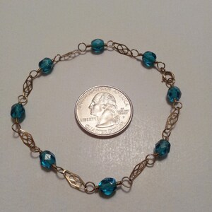 May include: A gold chain bracelet with teal blue faceted beads. The bracelet is about the size of a quarter.