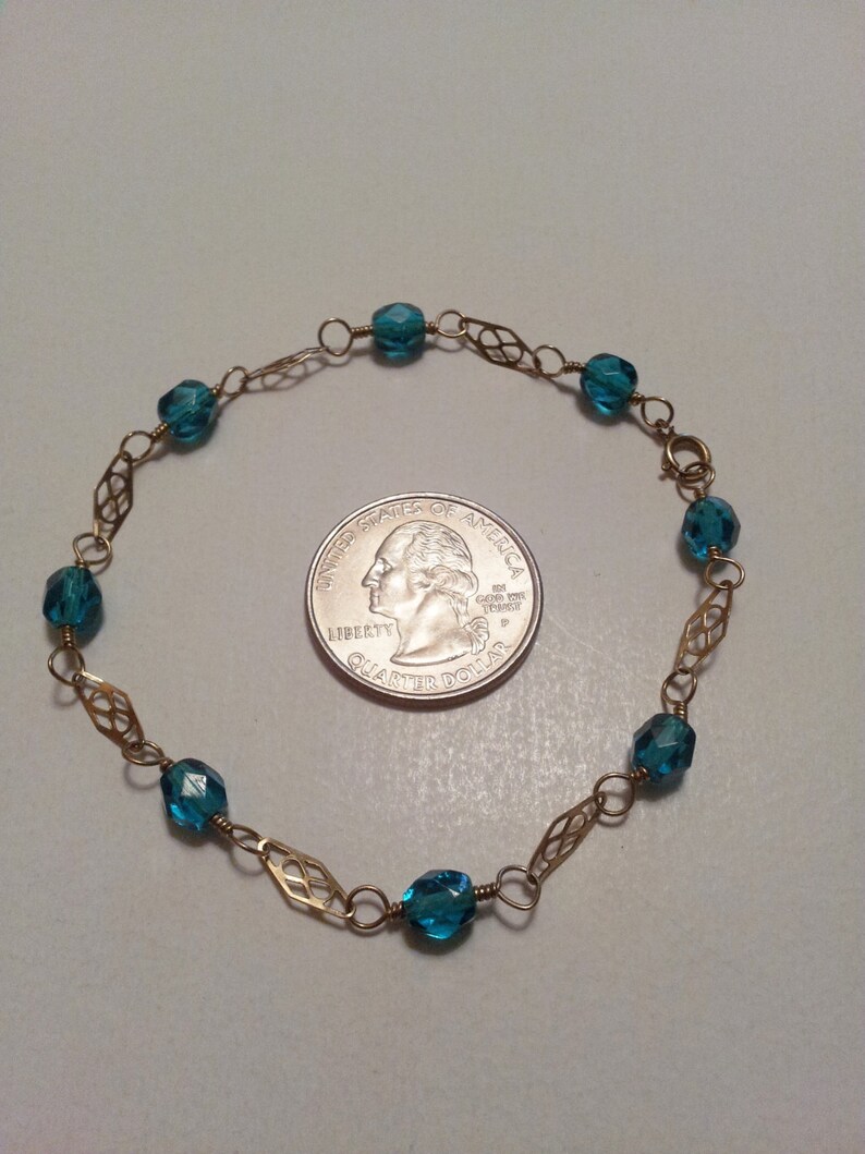 May include: A gold chain bracelet with teal blue faceted beads. The bracelet is about the size of a quarter.
