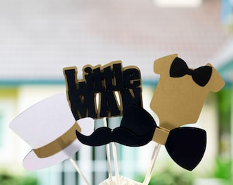 Könnte beinhalten: Ein Set aus Tortenaufsteckern bestehend aus einem weißen Zylinder mit goldenem Band, dem schwarzen Schriftzug "Little Man", einem schwarzen Schnurrbart und einem goldenen Babybody mit schwarzer Fliege, befestigt an dünnen weißen Stäbchen.