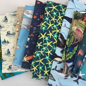 May include: A collection of ten fabric swatches featuring various ocean-themed patterns. The fabrics are in shades of blue, green, and white, and feature designs such as starfish, seahorses, and whales.