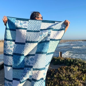May include: A rectangular patchwork quilt featuring a variety of blue and white fabric squares. The design incorporates multiple shades of blue, including navy, sky blue, and teal, arranged in a grid pattern with visible quilted stitching.