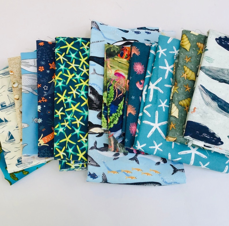 May include: A collection of 14 fabric squares featuring various ocean-themed designs. The fabrics are a mix of blue, green, and white with patterns of starfish, fish, whales, and seashells.