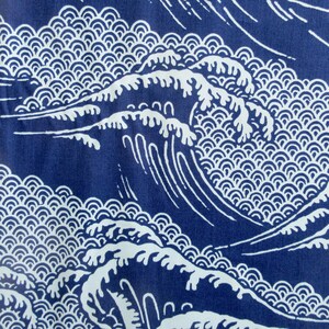 May include: A dark blue fabric featuring a repeating white graphic print of stylized ocean waves. The design consists of large, cresting wave forms layered over a background pattern of small, uniform, semi-circular scale shapes.