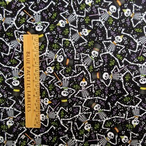 May include: Black fabric with a repeating pattern of white skeletons, musical notes, and confetti. Some skeletons wear top hats or party hats. A wooden ruler with inch measurements is on the left side of the image.