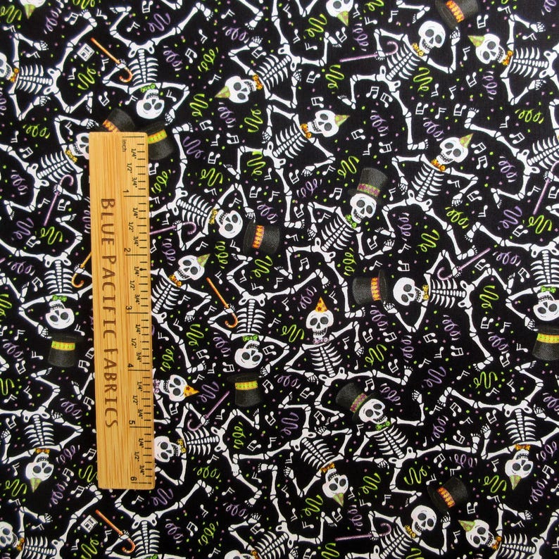May include: Black fabric with a repeating pattern of white skeletons, musical notes, and confetti. Some skeletons wear top hats or party hats. A wooden ruler with inch measurements is on the left side of the image.