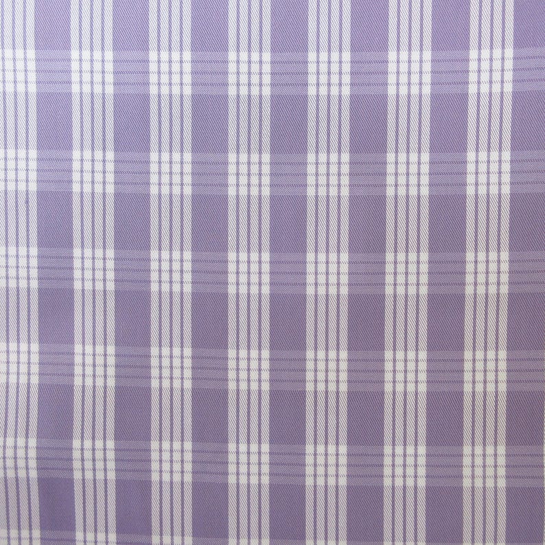 May include: A close-up of a fabric with a plaid pattern. The fabric features a light purple background with a grid of white and light purple lines. The lines intersect to create a classic plaid design, suitable for various textile applications.