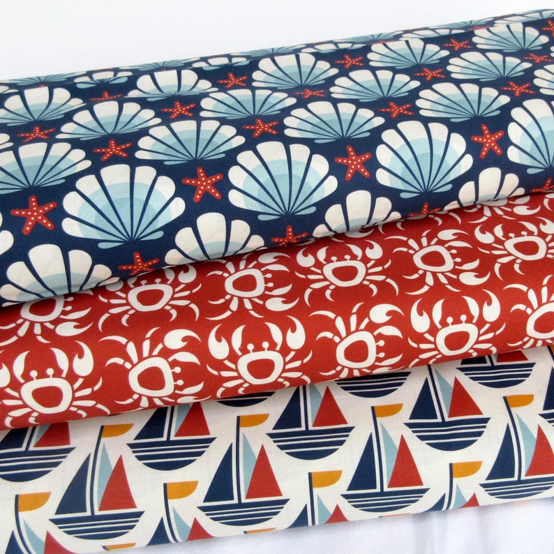 May include: Three fabric swatches with nautical themes. The top swatch is navy blue with white seashells and red starfish. The middle swatch is red with white crab silhouettes. The bottom swatch is white with blue and red sailboats.