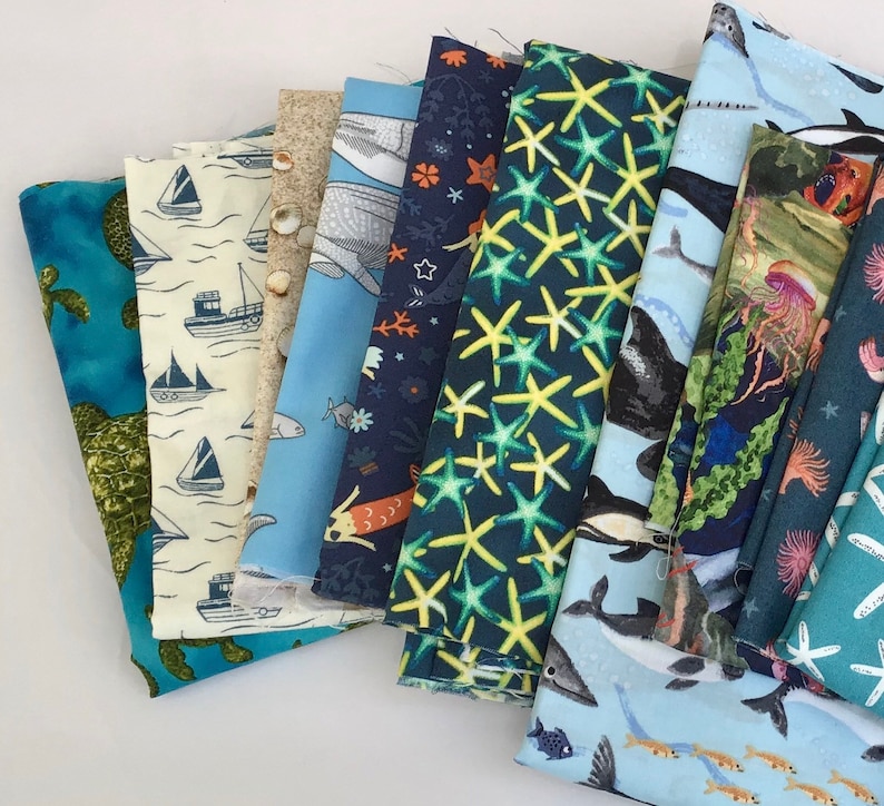 May include: A collection of ten fabric swatches featuring various ocean-themed patterns. The fabrics are in shades of blue, green, and white, and feature designs such as starfish, seahorses, and whales.