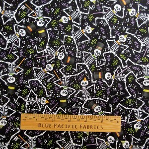 May include: Black fabric with a repeating pattern of white skeletons wearing hats and holding canes. The design includes musical notes and confetti in green and purple. A wooden ruler with "BLUE PACIFIC FABRICS" is at the bottom.
