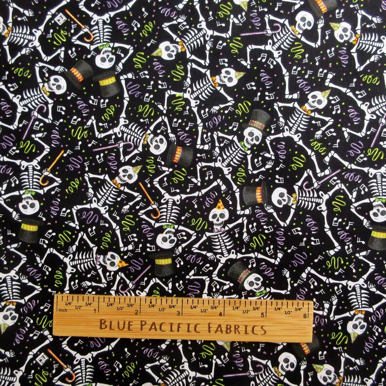 May include: Black fabric with a repeating pattern of white skeletons wearing hats and holding canes. The design includes musical notes and confetti in green and purple. A wooden ruler with "BLUE PACIFIC FABRICS" is at the bottom.