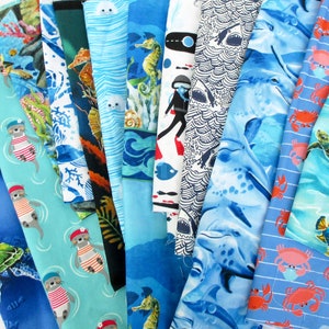 May include: A collection of 12 different fabric swatches featuring various ocean-themed patterns. The fabrics are in shades of blue, green, and white, and feature designs such as sea turtles, seahorses, dolphins, and crabs.