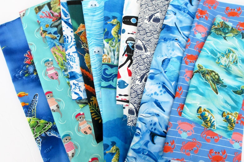 May include: A collection of 12 different fabric swatches featuring various ocean-themed patterns. The fabrics are in shades of blue, green, and white, and feature designs such as sea turtles, seahorses, dolphins, and crabs.