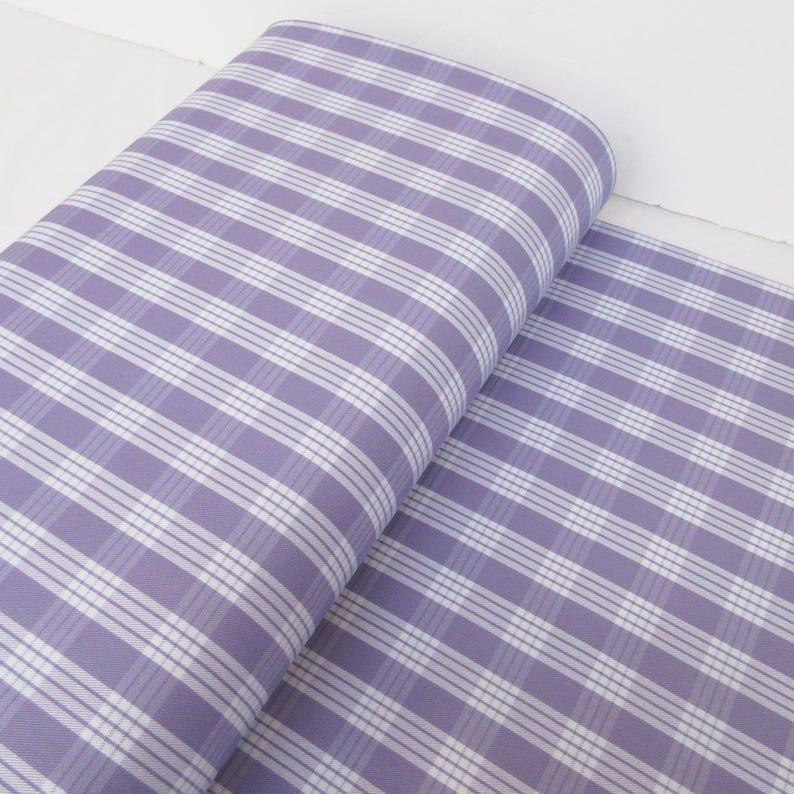 May include: A roll of fabric with a lavender and white plaid pattern. The fabric is rolled up, revealing the pattern of intersecting lines. The fabric is a light color and appears to be cotton or a similar material.