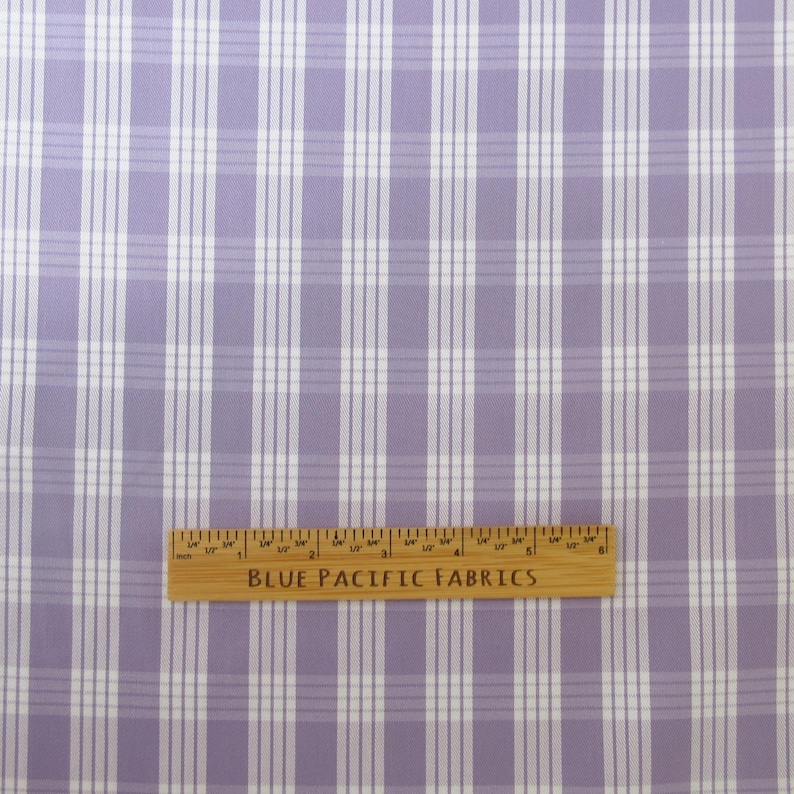 May include: A close-up of a fabric with a plaid pattern in shades of lavender and white. A wooden ruler with the text "BLUE PACIFIC FABRICS" is at the bottom of the image.