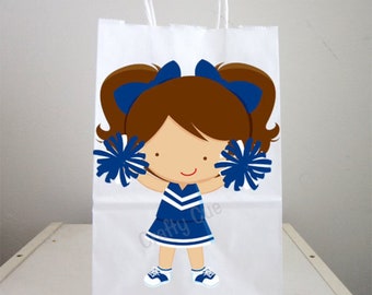 May include: White paper gift bag with a blue and white cheerleader girl graphic. The girl has brown hair, blue pom-poms, and a blue and white uniform.