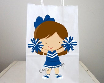 May include: White paper gift bag with a blue and white cheerleader girl graphic. The girl is holding pom-poms and has brown hair with a blue bow. The text "CRAFTY CUE" is printed on the bag.
