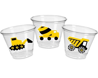 May include: Three clear plastic cups with yellow construction vehicle designs. The cups feature a yellow bulldozer, a yellow cement mixer, and a yellow dump truck.