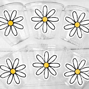 Pode incluir: Seis copos de pl&aacute;stico transparentes com desenhos de margaridas brancas e centros amarelos. As margaridas s&atilde;o contornadas a preto.