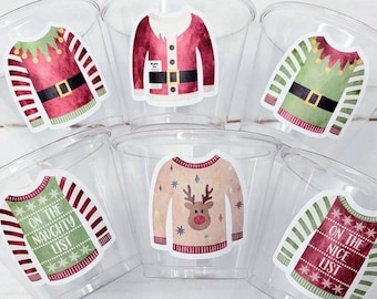 May include: Clear plastic cups with various Christmas sweater stickers. The stickers feature festive designs, including an elf sweater, a reindeer sweater, and sweaters with the phrases "On the Naughty List" and "On the Nice List."