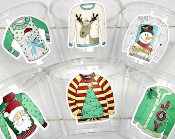 May include: Six clear plastic cups, each featuring a unique holiday-themed sweater sticker. Designs include a cat with a bow, a reindeer, a snowman with the text SNOWMAN, a Santa Claus with the text HO HO, a Christmas tree, and a green sweater with the text JOY.