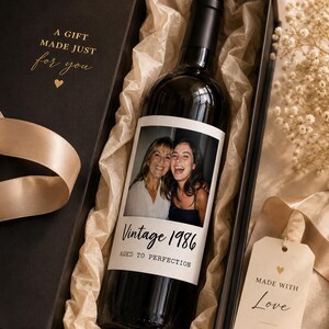 May include: A black gift box containing a dark glass wine bottle with a custom photo label featuring two people. The label reads Vintage 1986 AGED TO PERFECTION. The box interior has gold text A GIFT MADE JUST for you and a tag reading MADE WITH Love.