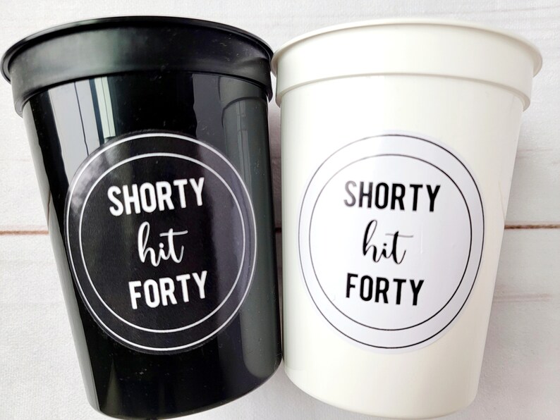 May include: Two plastic cups, one black and one white, with the text "SHORTY hit FORTY" on a circular sticker. The cups are likely for a party or event, with a celebratory theme.