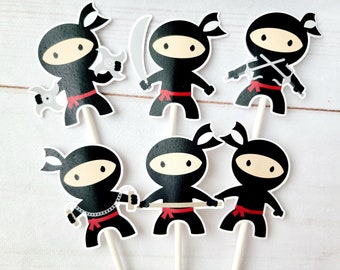 May include: Six black and white ninja cupcake toppers with red sashes. Each topper features a different ninja weapon, including a sword, a shuriken, and a sai.