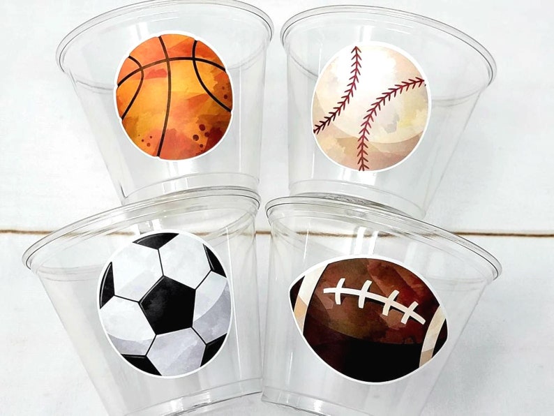 May include: Four clear plastic cups with sports-themed stickers. The stickers feature a basketball, baseball, soccer ball, and football. The basketball is orange and brown, the baseball is white and red, the soccer ball is black and white, and the football is brown and white.

SPORTS PARTY CUPS - Sports Cups Sports Birthday Sports Party Football Party Cups Baseball Party Cups Soccer Party Cups Basketball Party Cups