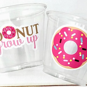 May include: Two clear plastic cups with donut-themed designs. One cup has a pink donut with sprinkles and the text "DONUT grow up". The other cup has a pink donut with sprinkles.