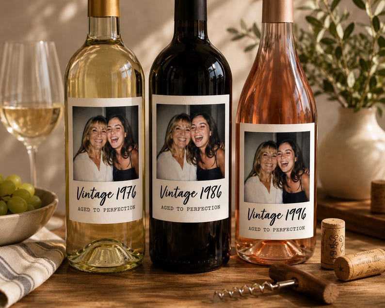 May include: Three glass wine bottles with custom labels featuring a photograph of two smiling people. The labels display the text Vintage 1976, 1986, and 1996, followed by the phrase AGED TO PERFECTION. The bottles contain white, red, and rose wine.