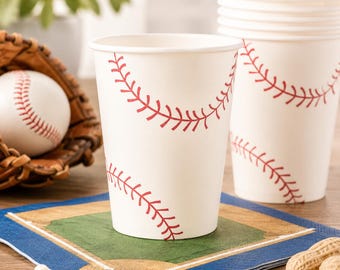 May include: White paper cups featuring a red baseball stitch pattern. The cups are arranged on a square paper napkin printed with a baseball diamond graphic. A brown leather baseball glove holding a white baseball is positioned nearby.