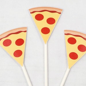 Puede incluir: Tres toppers de cupcake de papel en forma de rebanada de pizza amarilla y roja con palitos blancos.
