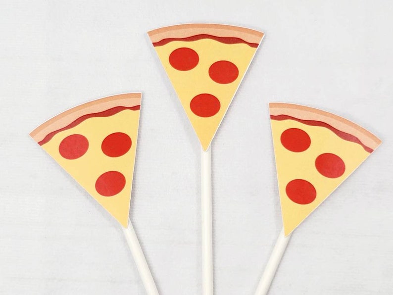 Puede incluir: Tres toppers de cupcake de papel en forma de rebanada de pizza amarilla y roja con palitos blancos.