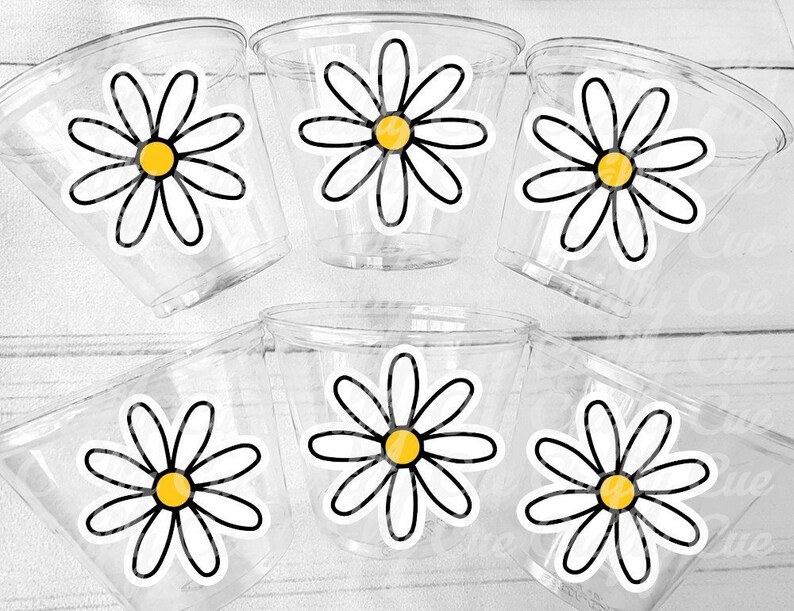 Pode incluir: Seis copos de pl&aacute;stico transparentes com desenhos de margaridas brancas e centros amarelos. As margaridas s&atilde;o contornadas a preto.