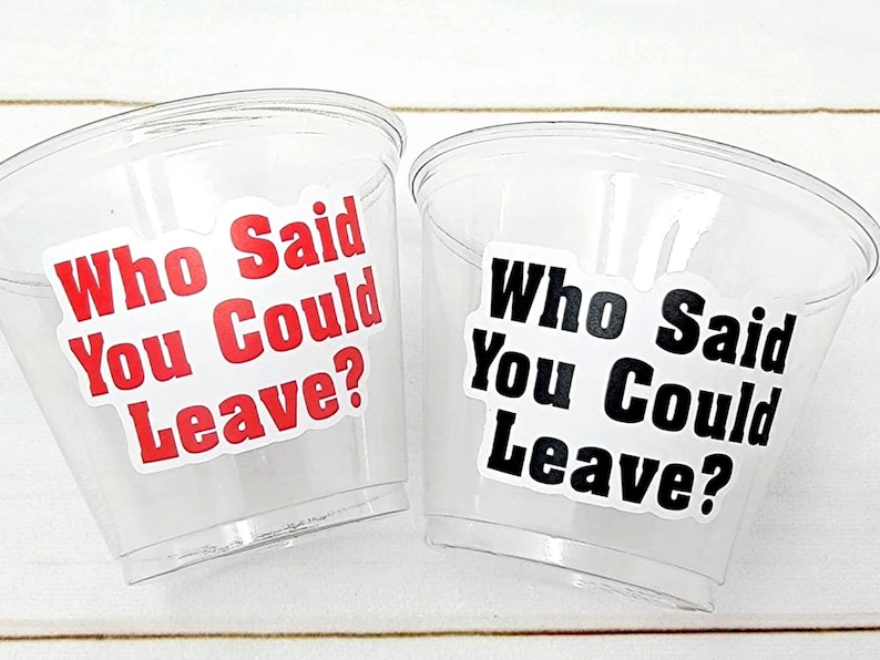 Puede incluir: Dos vasos de pl&aacute;stico transparente con pegatinas que dicen "Who Said You Could Leave?" en texto rojo y negro. Los vasos est&aacute;n sobre una superficie de madera blanca.