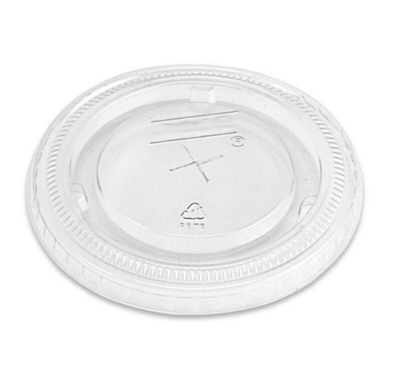 May include: Clear plastic lid for a cup or container. The lid has a raised edge and a smooth, flat surface. The lid is marked with a recycling symbol and the number "5".
