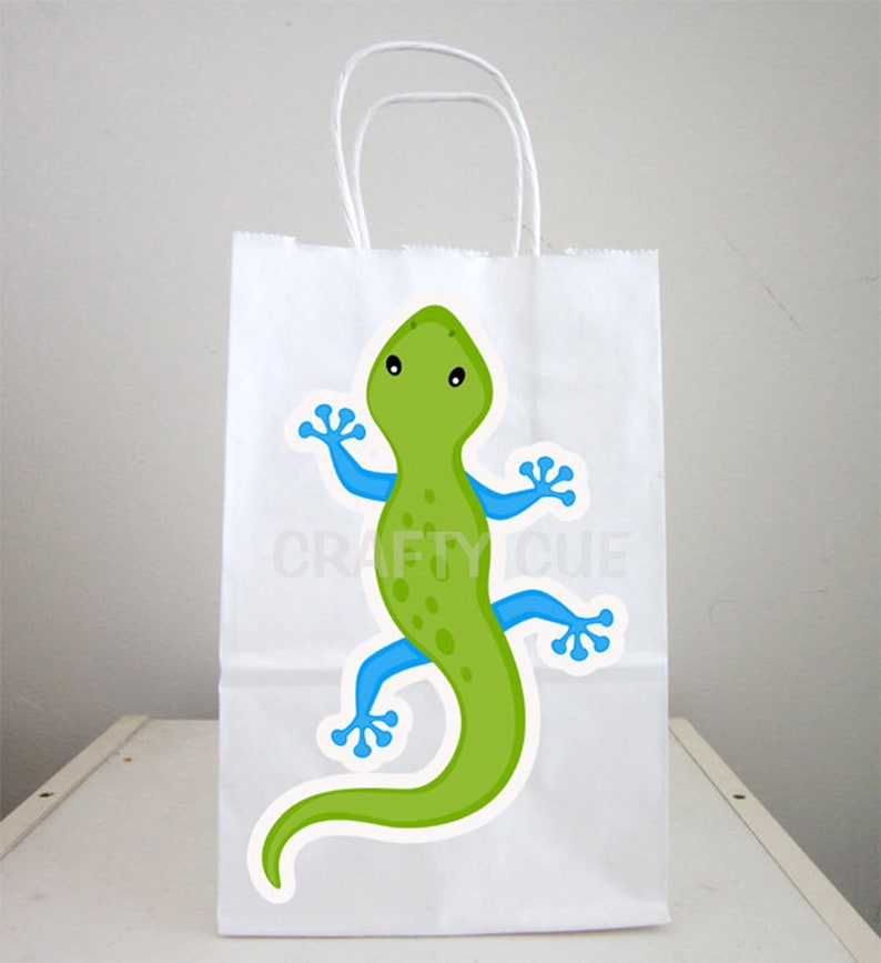 May include: White paper gift bag featuring a green gecko with blue limbs and black eyes. The gecko is facing forward with its arms and legs outstretched.